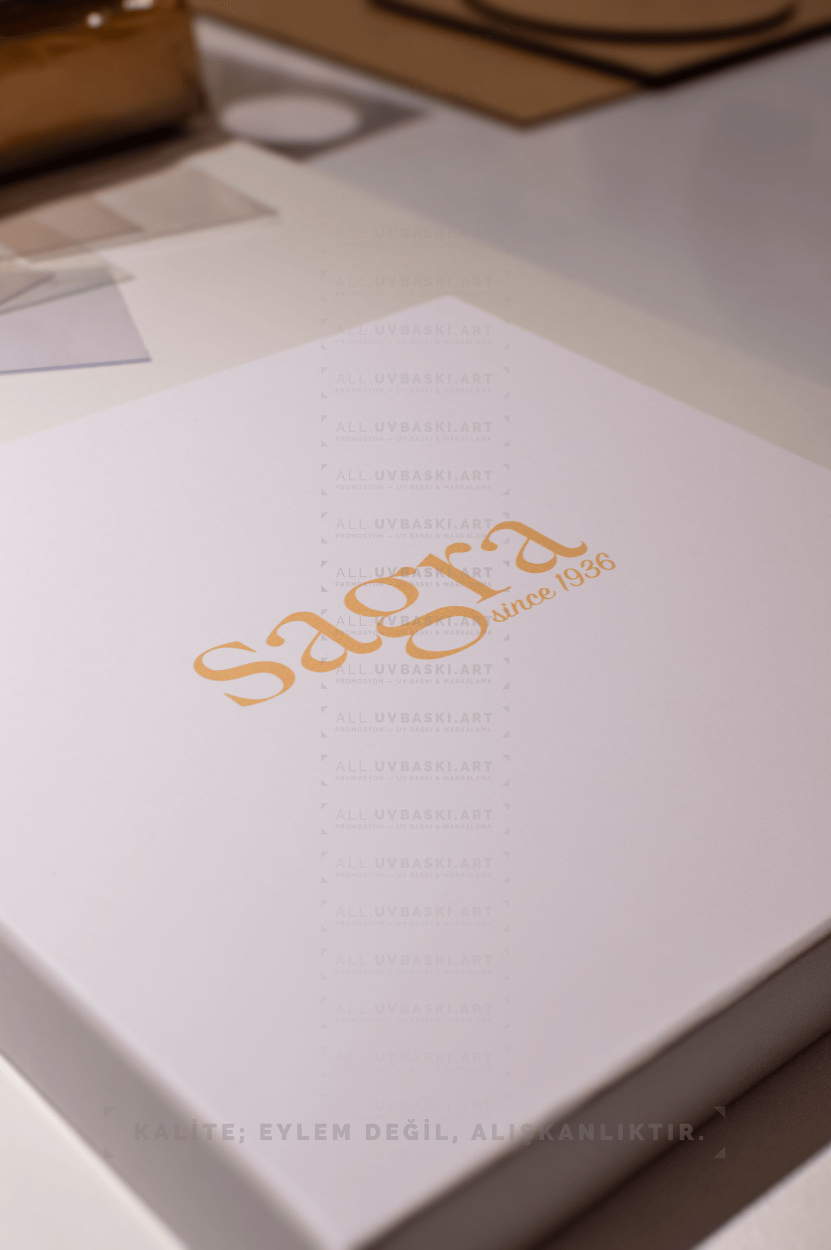 Beyaz kutu kapağı üzerine sarı ve altın tonlarında Sagra logosu UV baskısı.