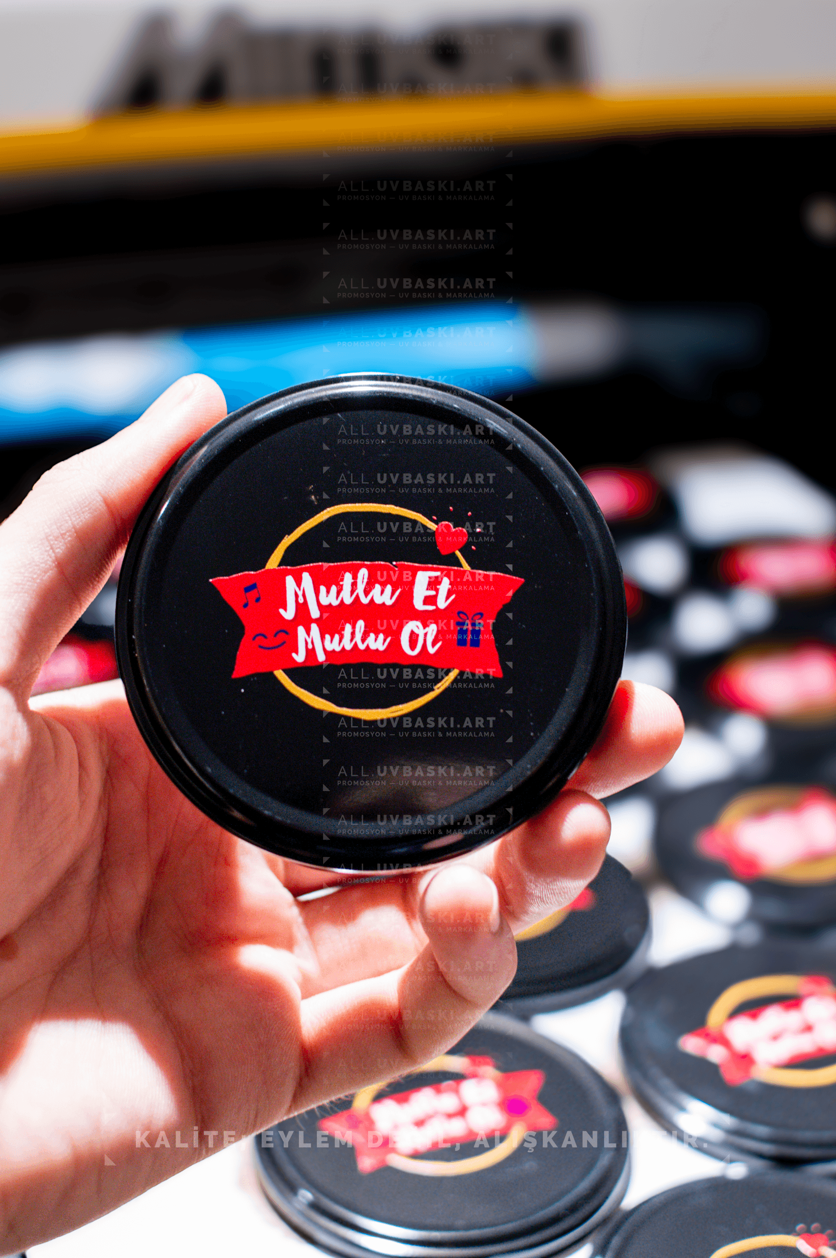 Siyah kavanoz kapağı üzerine Ülker Mutlu et, mutlu ol motto logosu, UV baskı örneği.